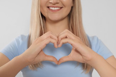 Photo of Happy volunteer making heart with her hands on light background, closeup