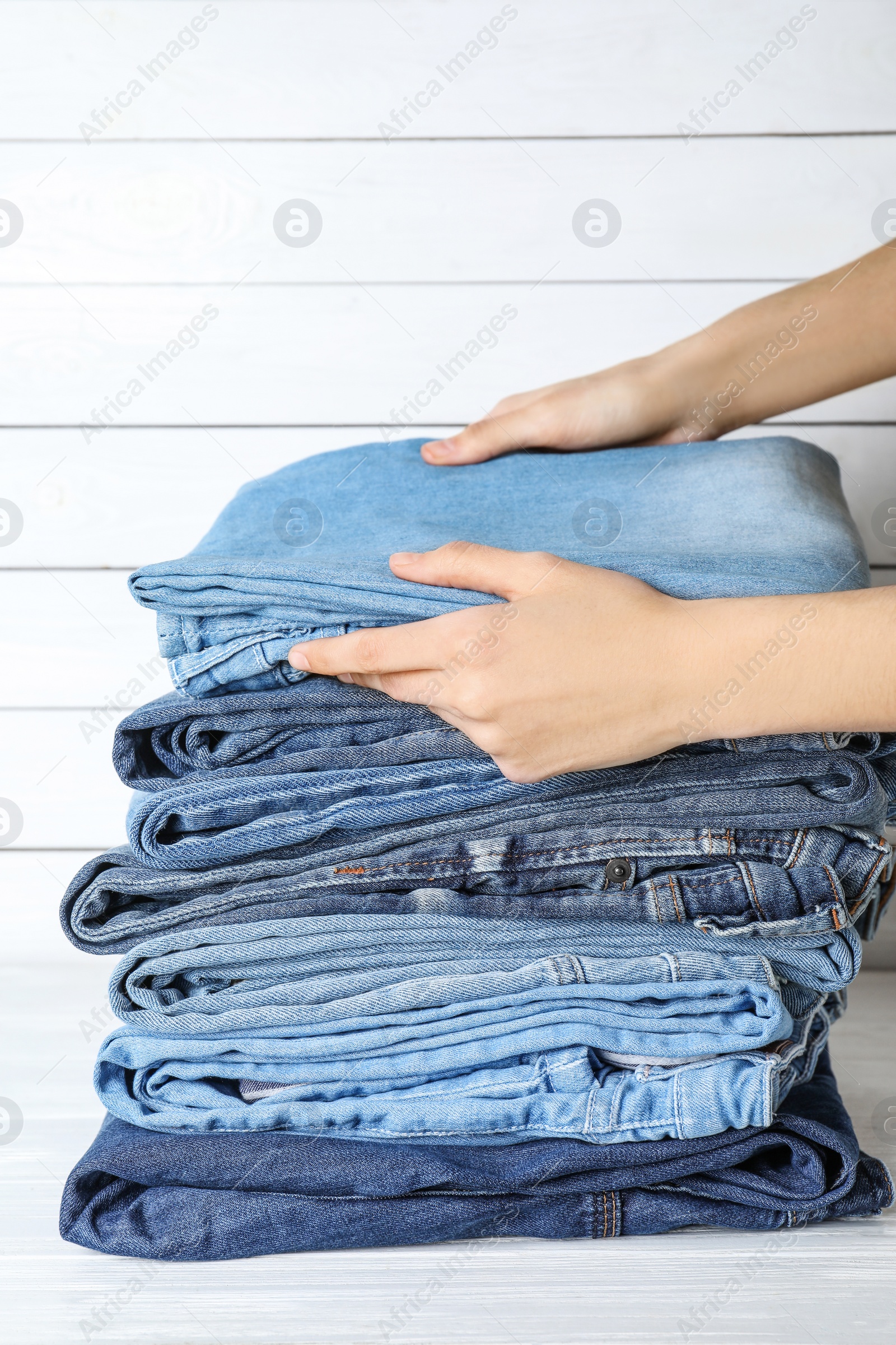 Photo of Woman folding stylish jeans on white wooden table, closeup