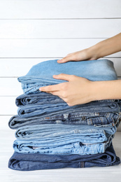 Woman folding stylish jeans on white wooden table, closeup