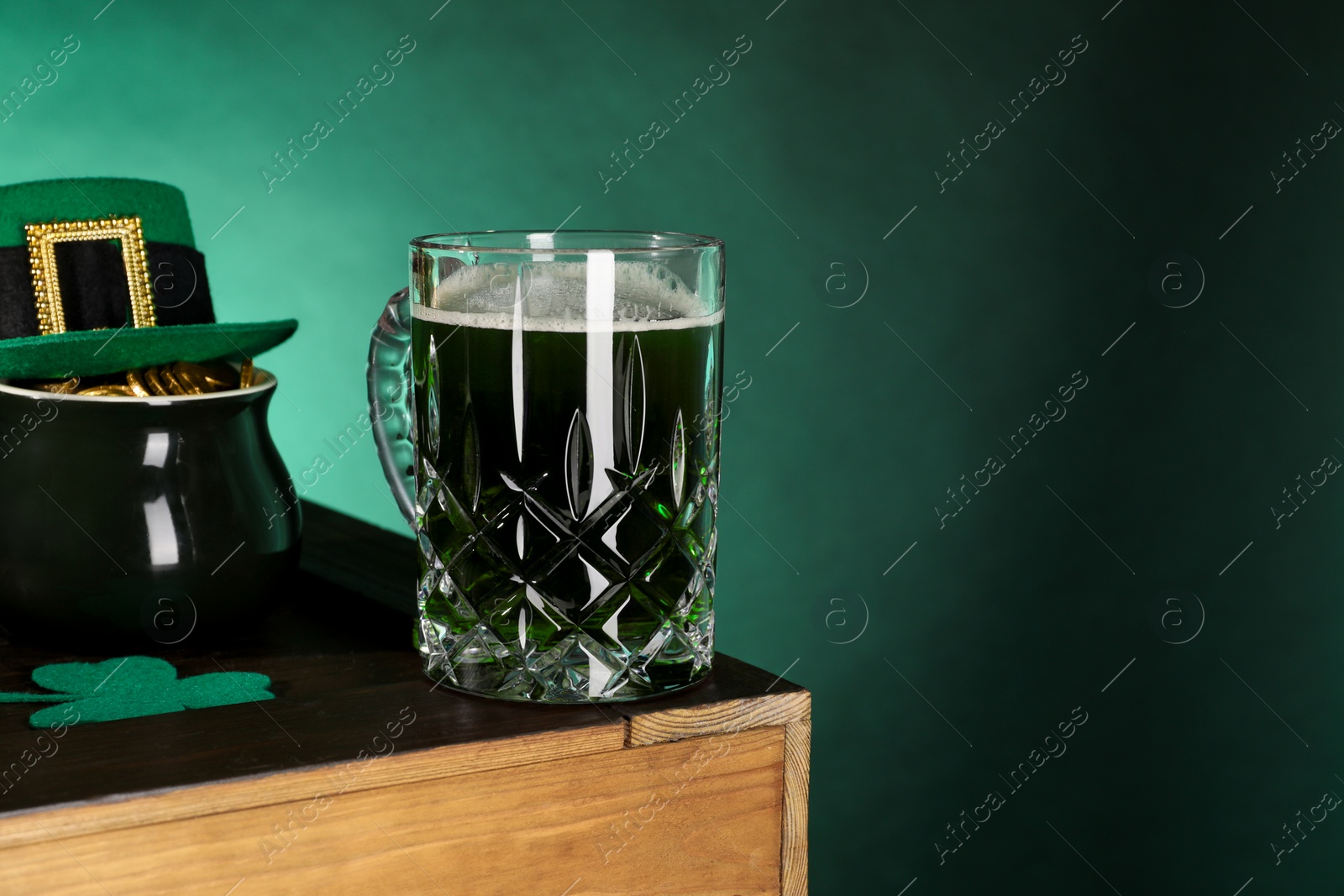 Photo of St. Patrick's day celebration. Green beer, leprechaun hat, pot of gold and decorative clover leaf on wooden table. Space for text