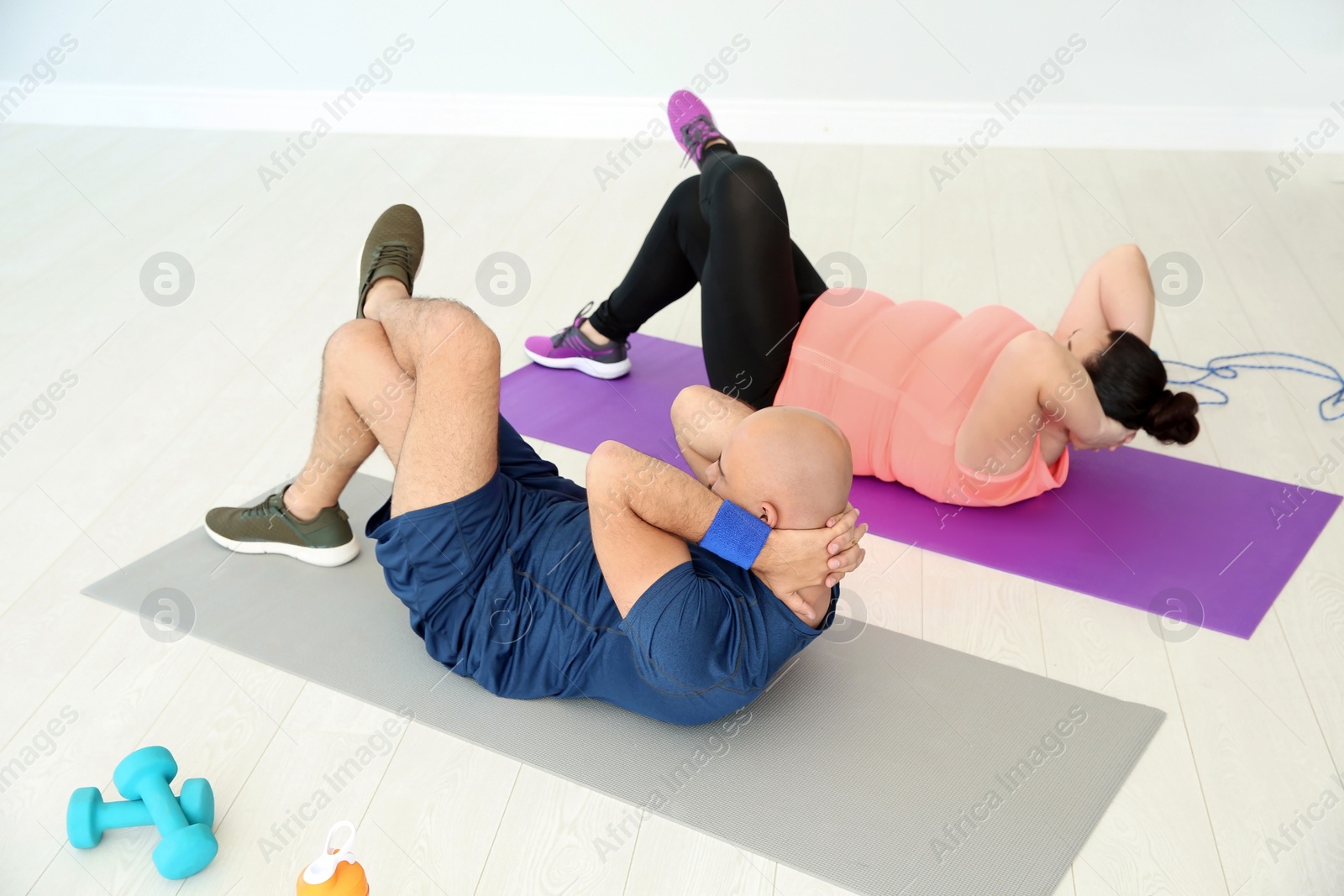 Photo of Overweight man and woman doing exercise on mats in gym