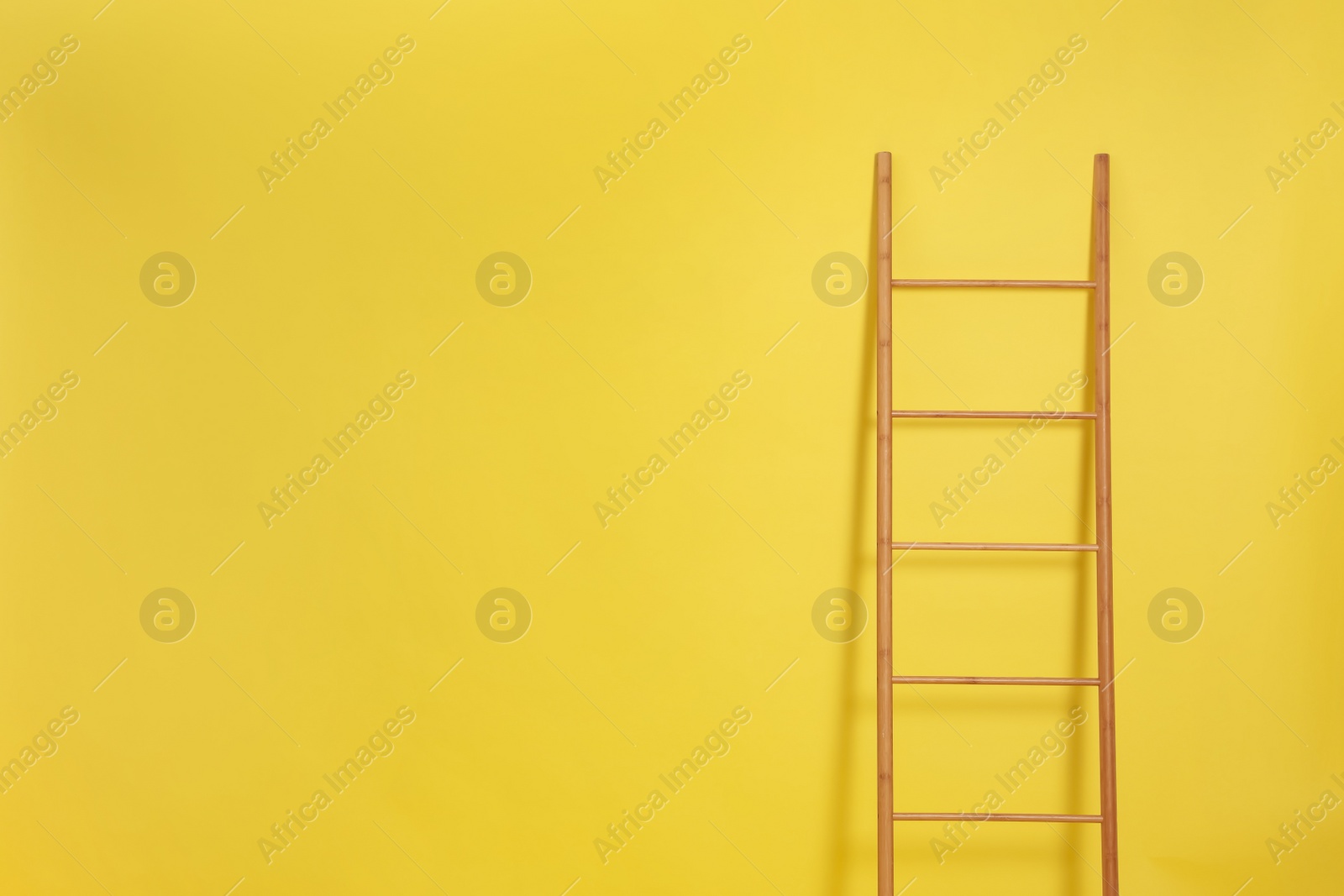 Photo of Modern wooden ladder on yellow background. Space for text