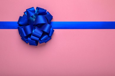 Photo of Blue ribbon with bow on pink background, top view. Space for text