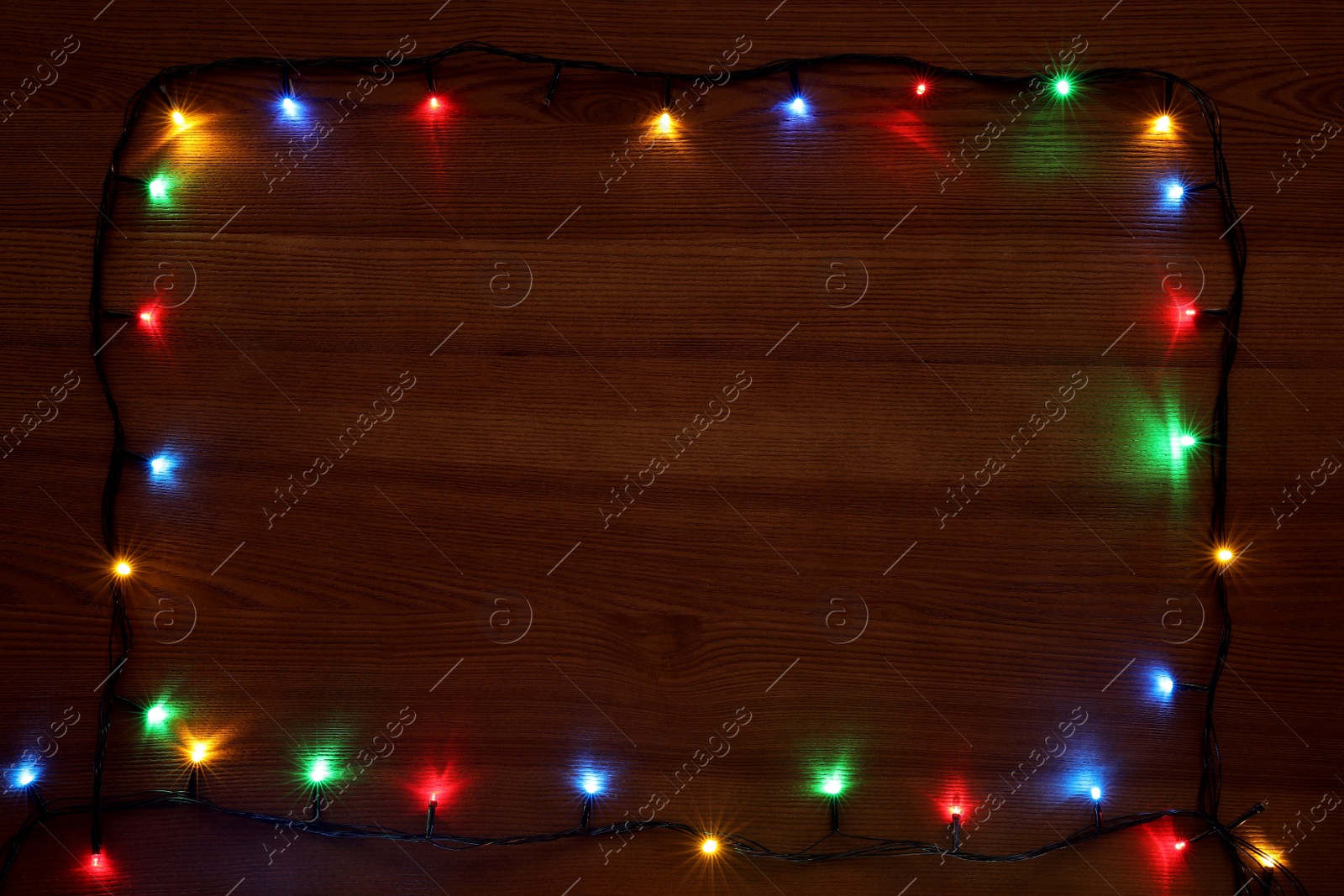 Photo of Frame of colorful Christmas lights on wooden table, top view. Space for text