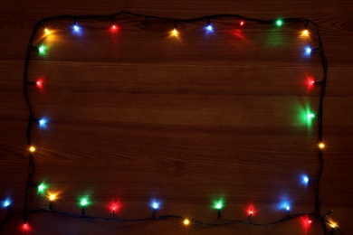 Photo of Frame of colorful Christmas lights on wooden table, top view. Space for text