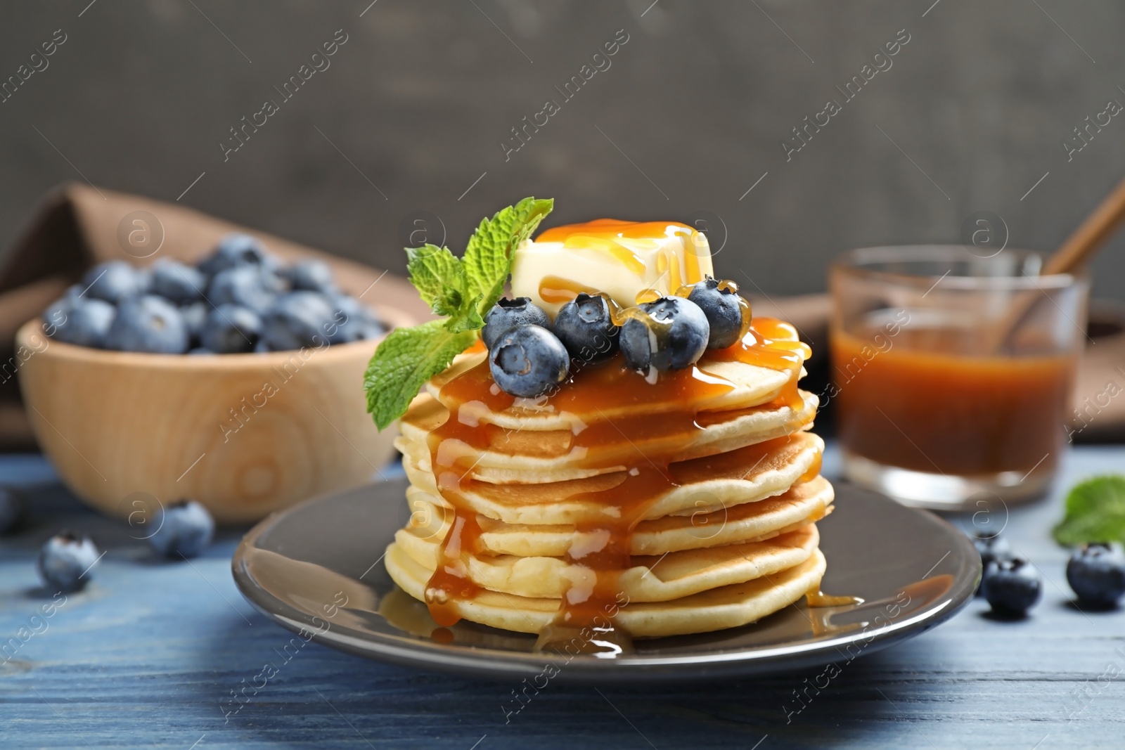 Photo of Delicious pancakes with fresh blueberries, butter and syrup on blue wooden table