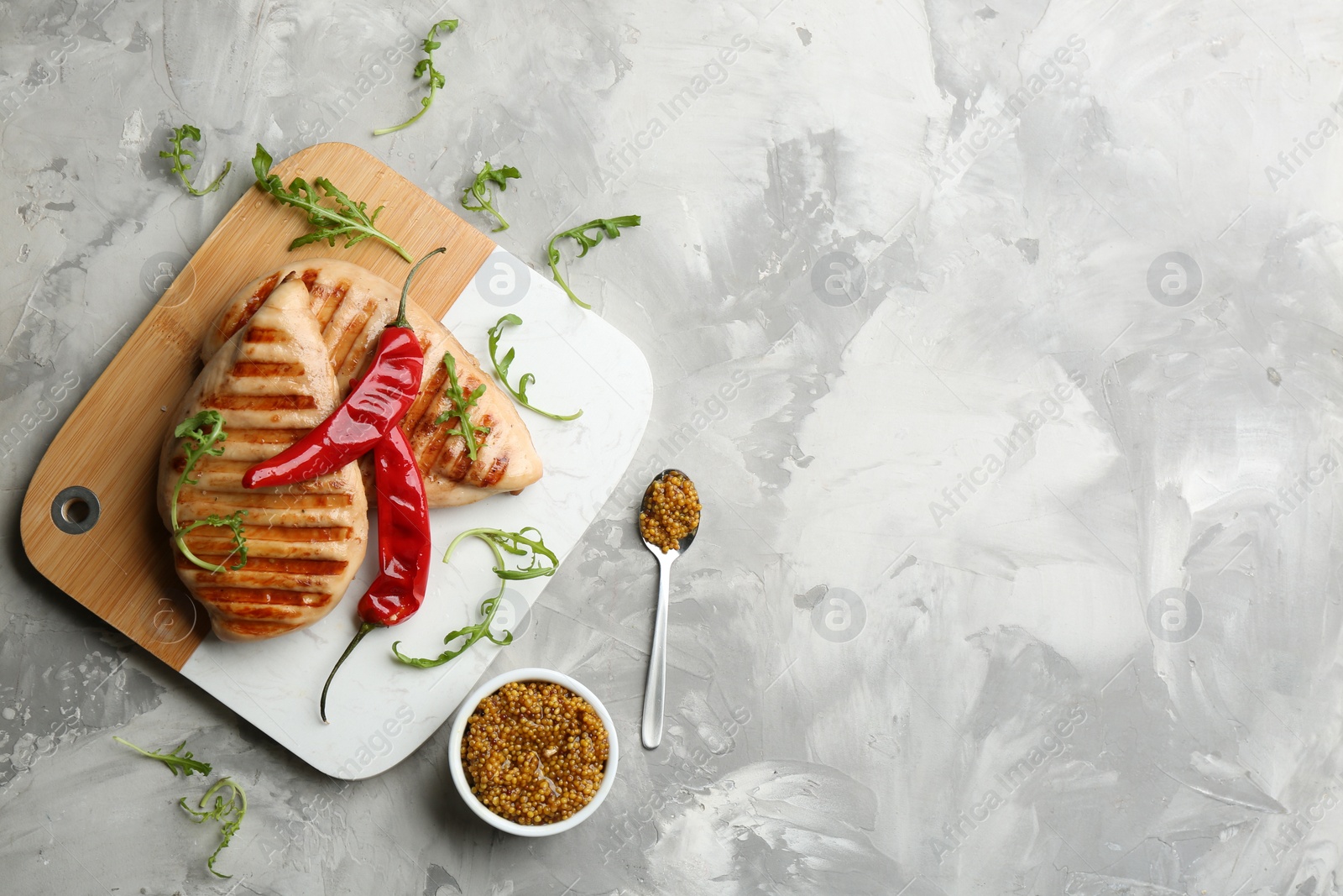Photo of Tasty grilled chicken fillets with mustard, chili peppers and arugula on light grey table, flat lay. Space for text