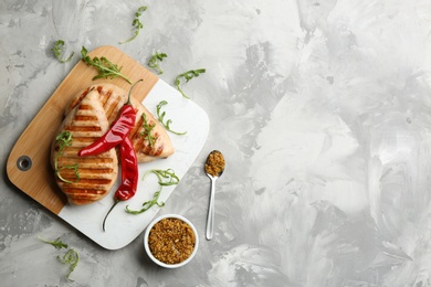 Photo of Tasty grilled chicken fillets with mustard, chili peppers and arugula on light grey table, flat lay. Space for text