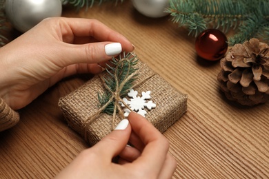 Photo of Woman wrapping Christmas gift at wooden table, closeup