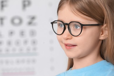 Photo of Little girl with glasses against vision test chart, closeup