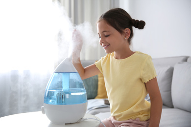 Little girl near modern air humidifier at home