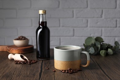 Bottle with delicious syrup, mug of aromatic coffee and beans on wooden table