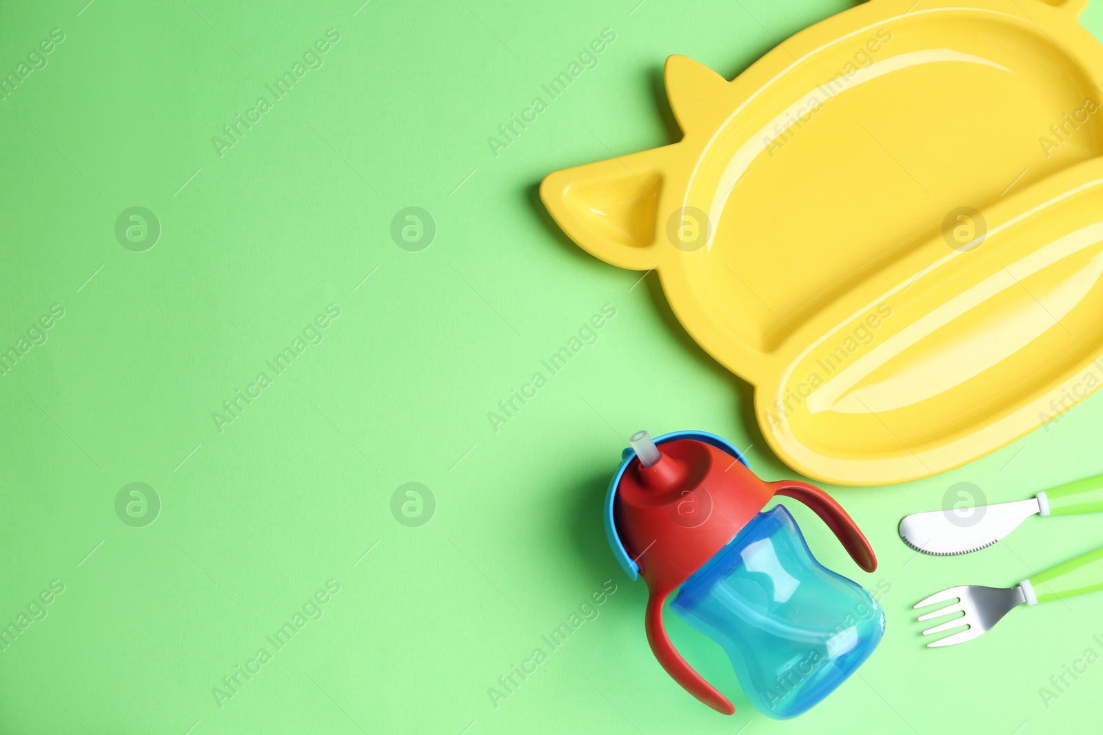 Photo of Set of colorful dishware on light green background, flat lay with space for text. Serving baby food