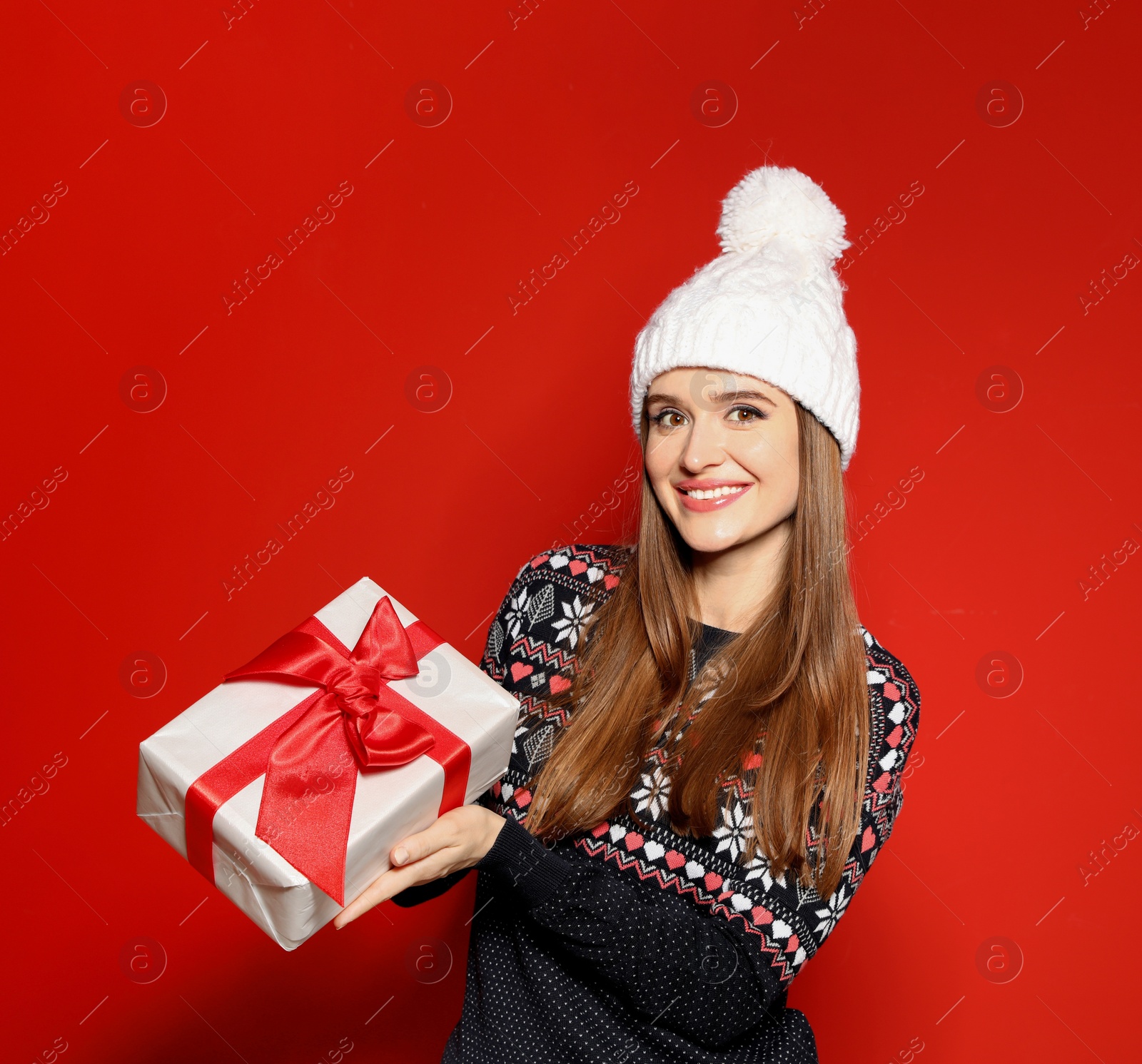 Photo of Young woman in Christmas sweater holding gift box on red background