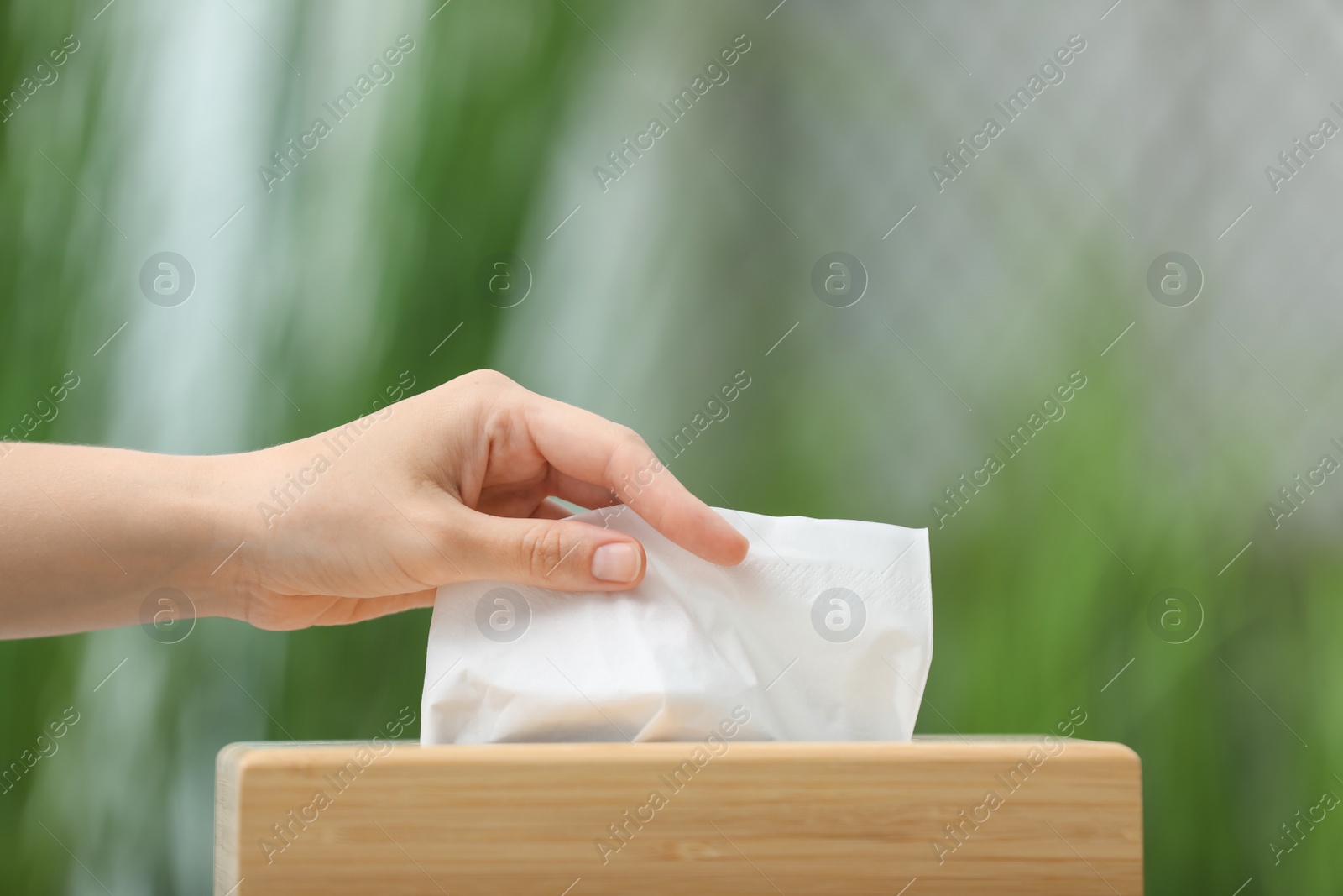 Photo of Woman taking paper tissue from holder on blurred background, closeup