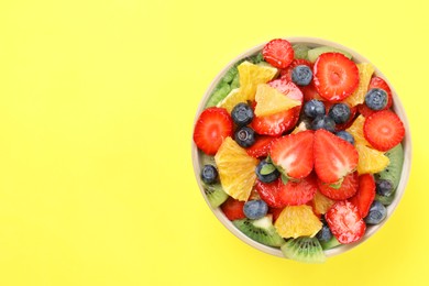 Yummy fruit salad in bowl on yellow background, top view. Space for text