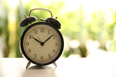 Modern black alarm clock on white table against blurred background. Space for text