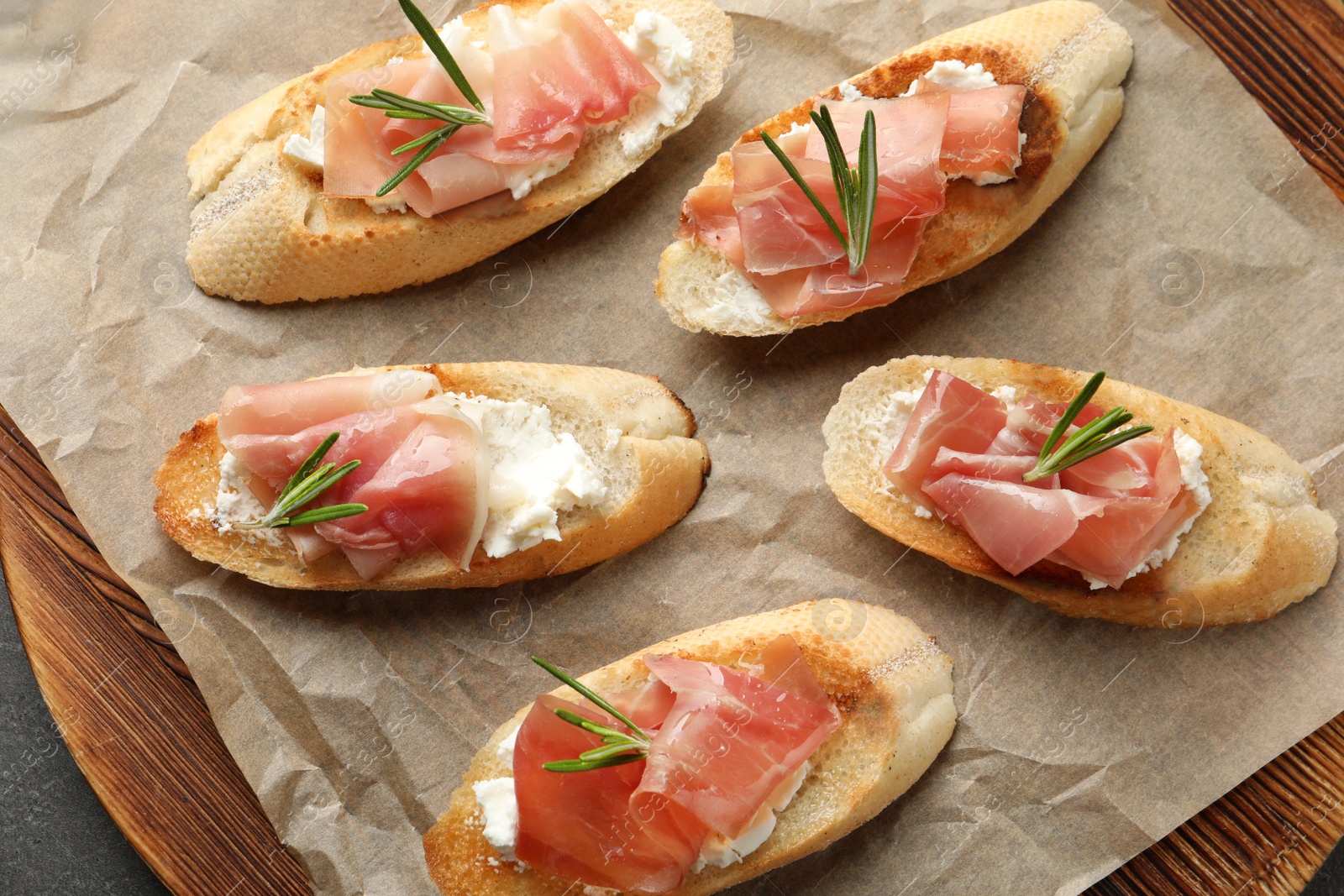 Photo of Tasty bruschettas with prosciutto and cream cheese on wooden board, top view