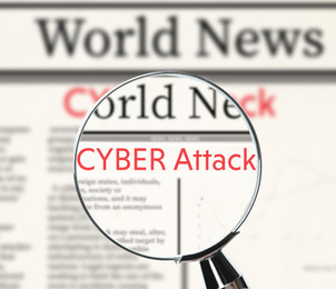 Image of Newspaper with headline CYBER ATTACK under magnifying glass, closeup