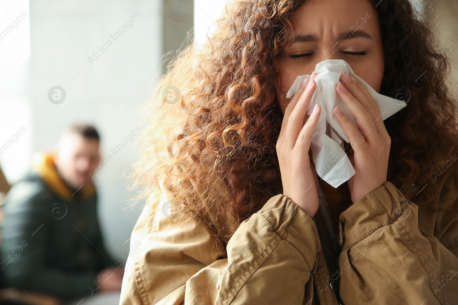 Photo of Young African-American woman sneezing indoors. Influenza virus