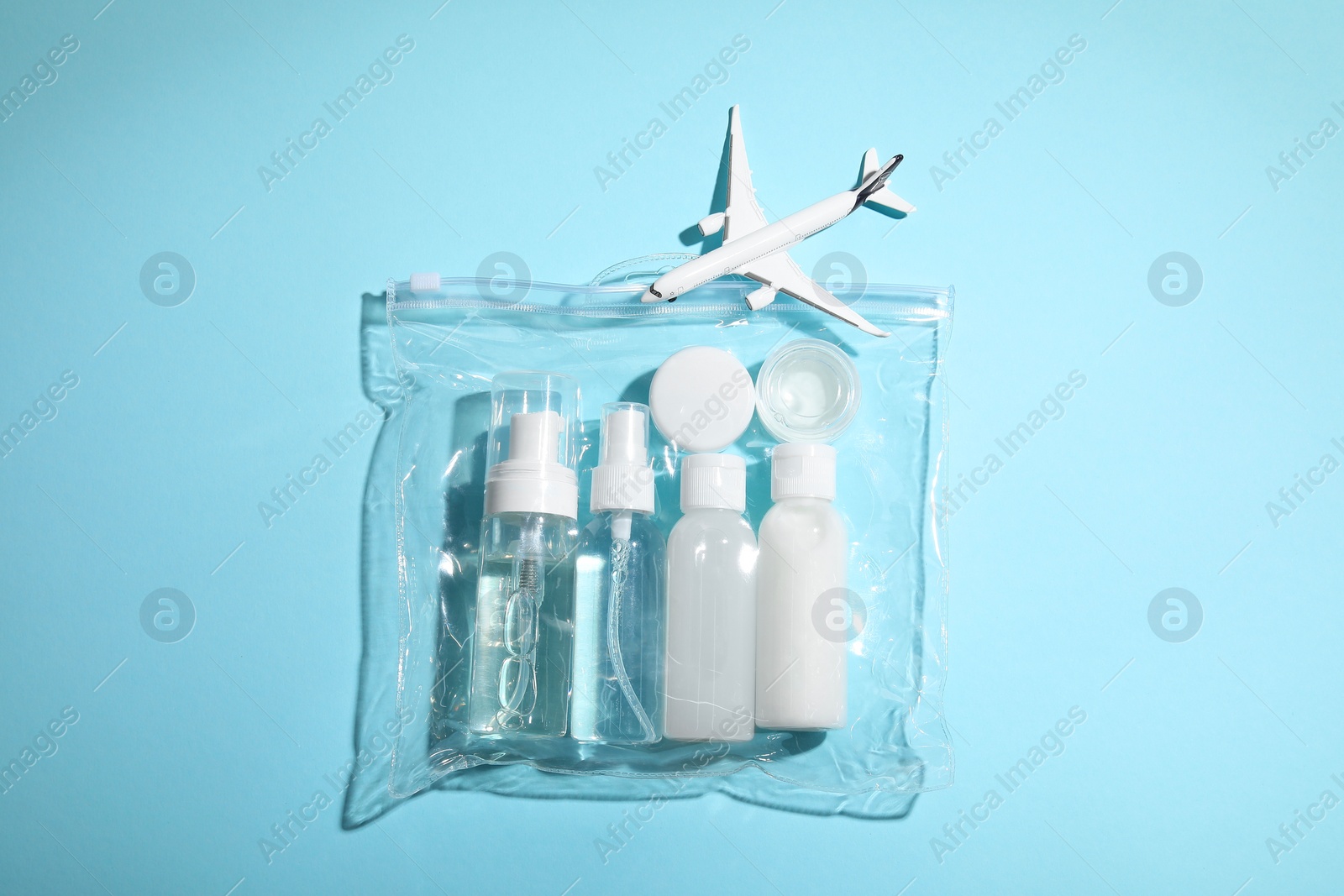 Photo of Cosmetic travel kit in plastic bag and toy plane on light blue background, top view. Bath accessories