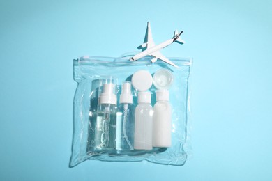 Cosmetic travel kit in plastic bag and toy plane on light blue background, top view. Bath accessories
