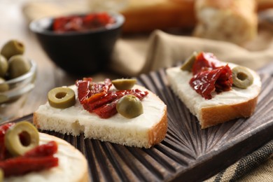 Delicious bruschettas with ricotta cheese, sun dried tomatoes and olives on table, closeup