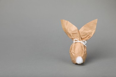 Photo of Easter bunny made of kraft paper and egg on grey background. Space for text