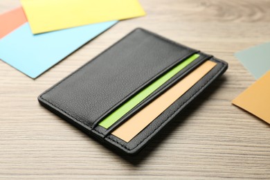 Leather business card holder with colorful cards on wooden table, closeup