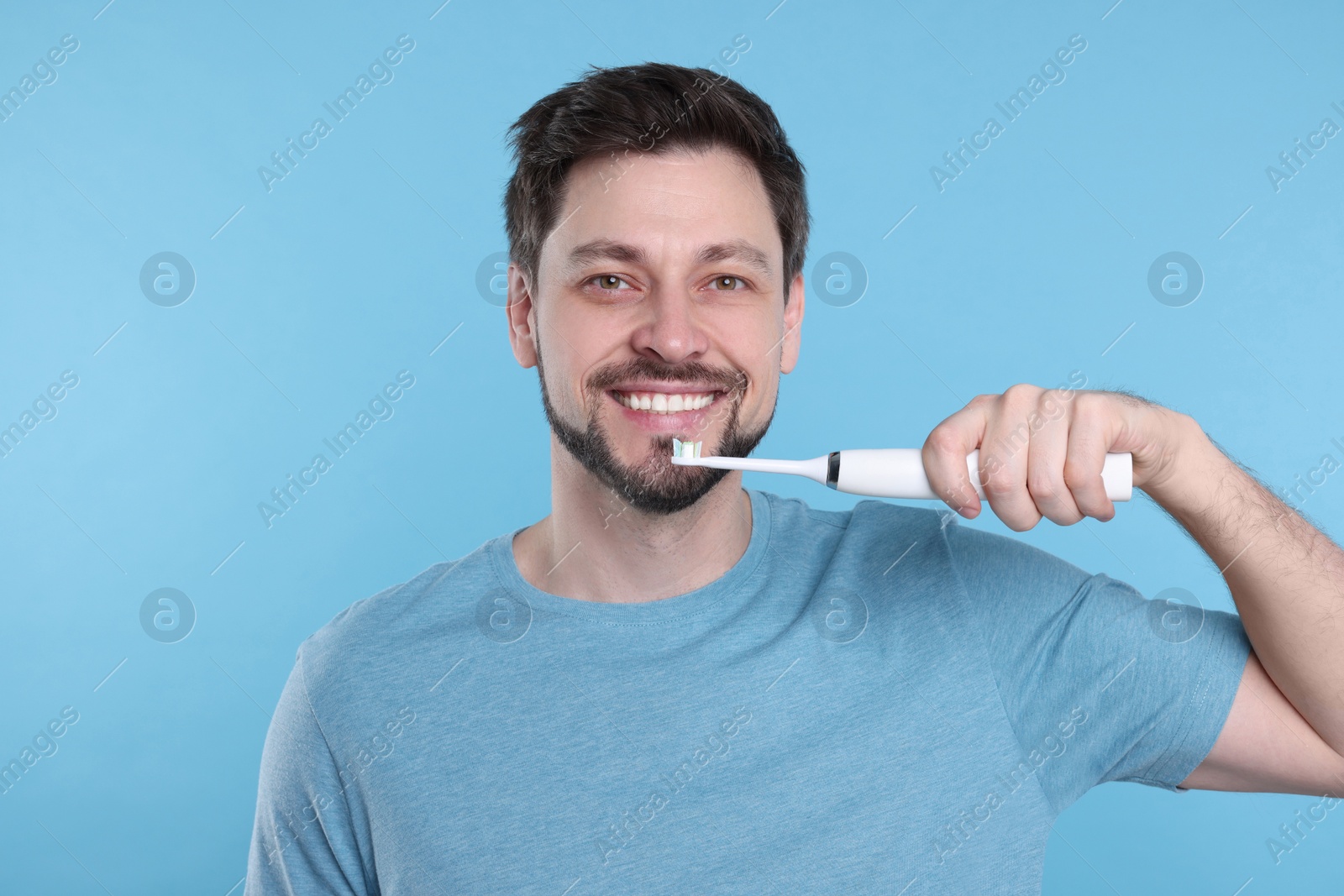 Photo of Happy man holding electric toothbrush on light blue background