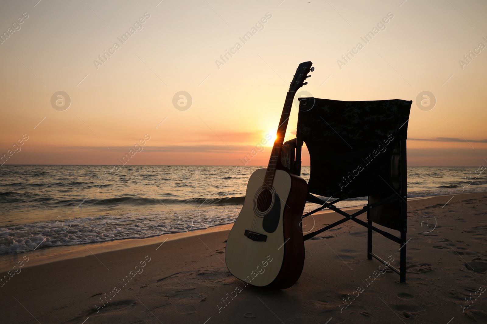 Photo of Camping chair and guitar on sandy beach near sea, space for text