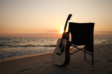 Photo of Camping chair and guitar on sandy beach near sea, space for text