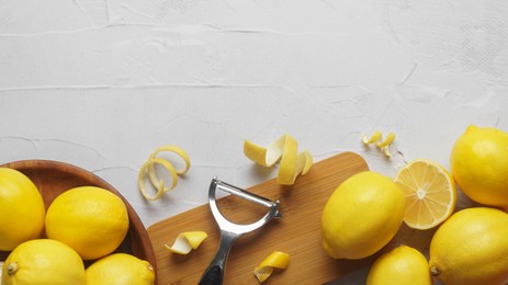 Photo of Wooden board, lemons, peeler and fresh rind on white textured table, flat lay. Space for text