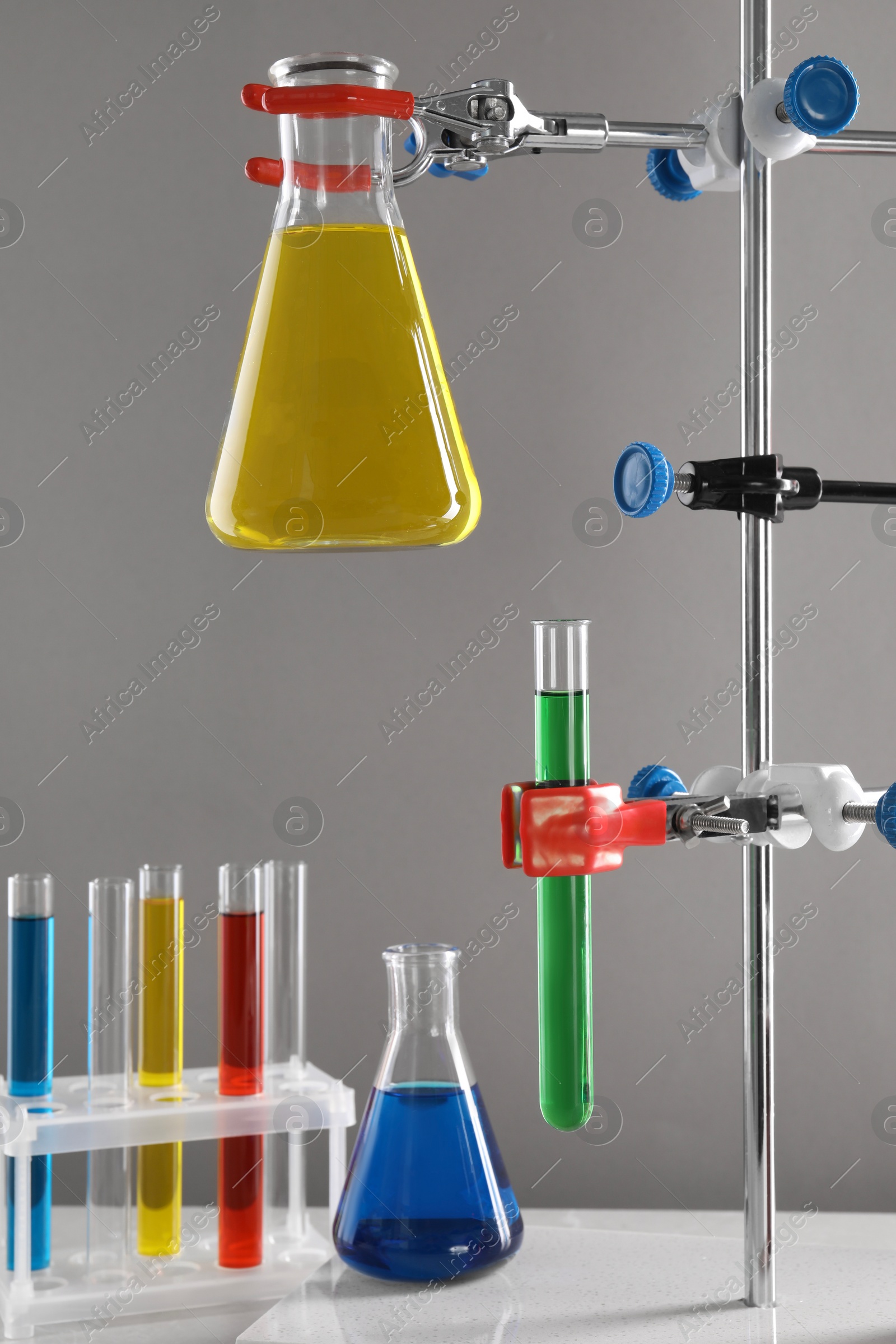 Photo of Retort stand and laboratory glassware with liquids on table against light grey background