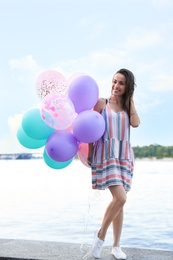 Photo of Pretty young woman with color balloons near river