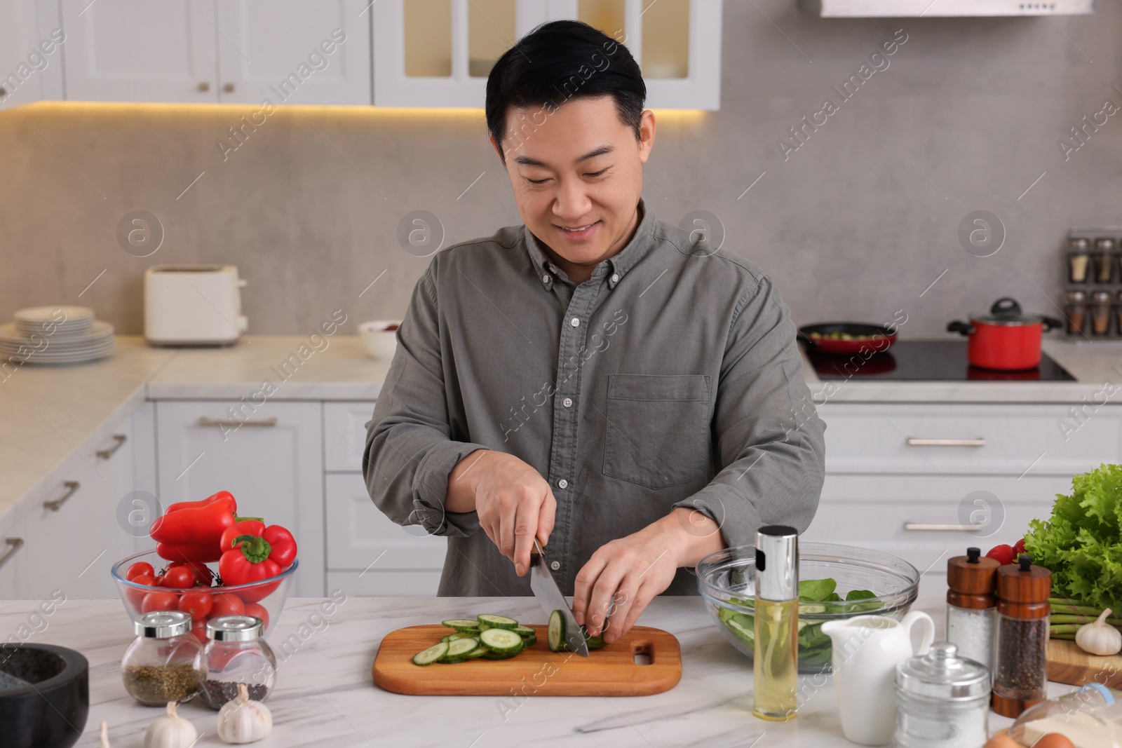 Photo of Cooking process. Man cutting fresh cucumber at countertop in kitchen