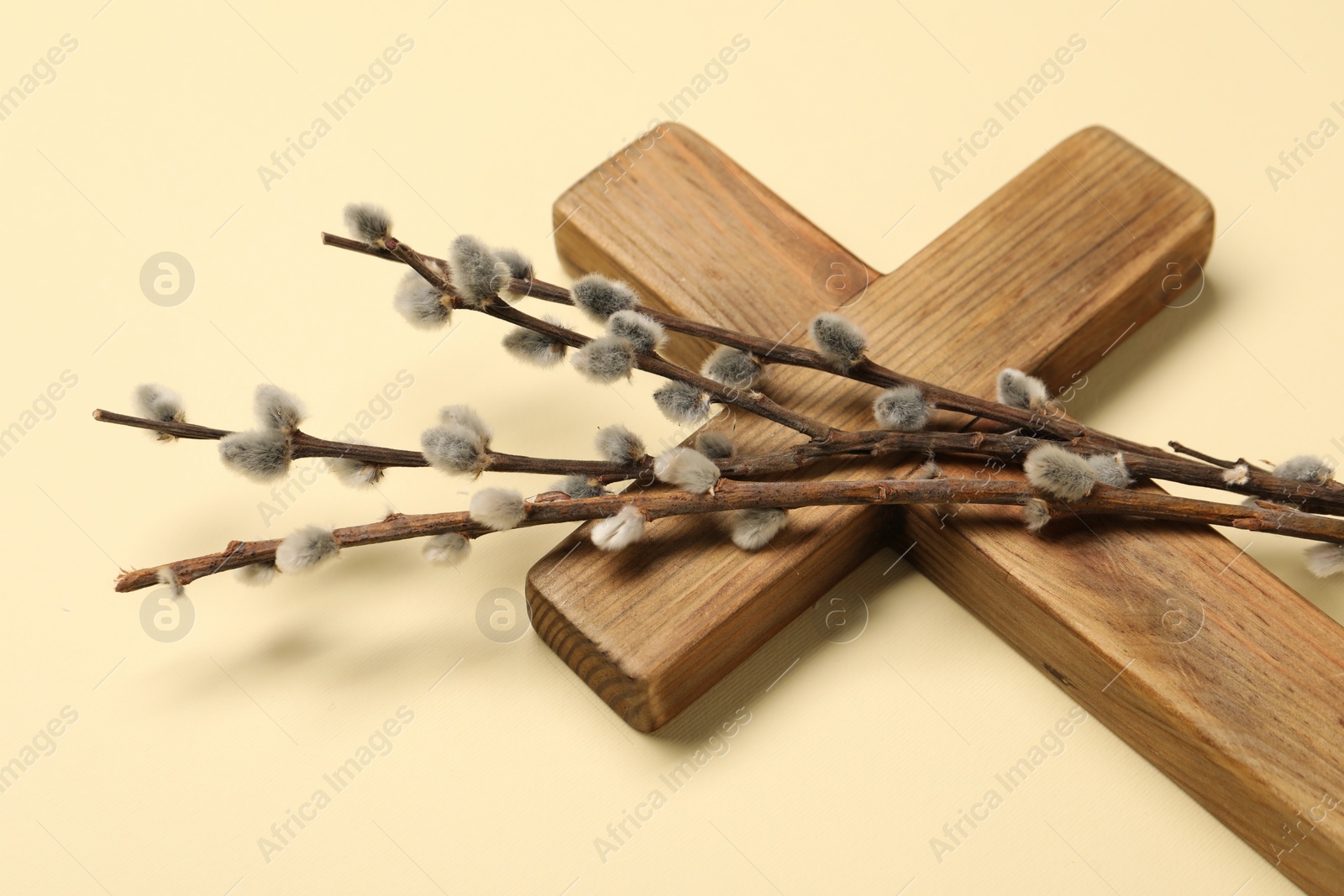 Photo of Wooden cross and willow branches on beige background, closeup. Easter attributes