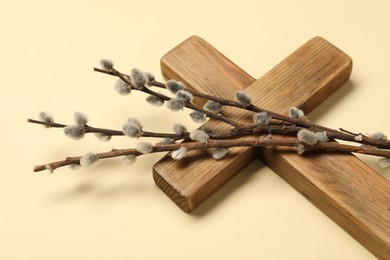 Wooden cross and willow branches on beige background, closeup. Easter attributes