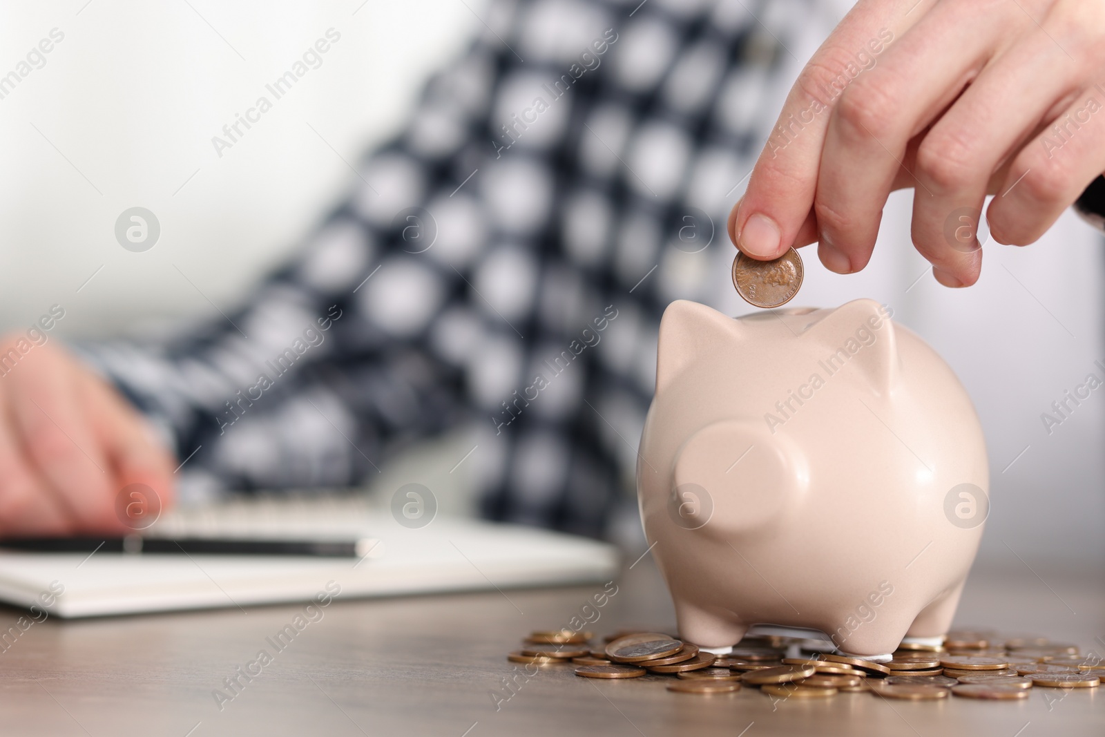 Photo of Financial savings. Man putting coin into piggy bank at wooden table, closeup