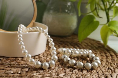 Photo of Stylish jewelry with pearls and box on wicker mat, closeup