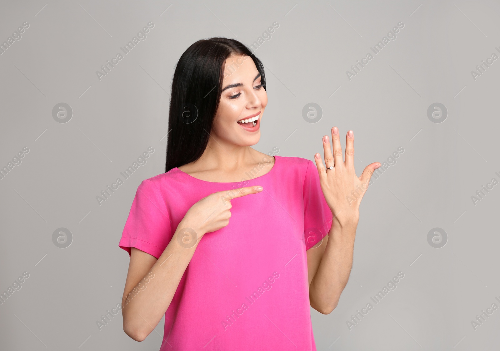 Photo of Happy young woman wearing beautiful engagement ring on grey background