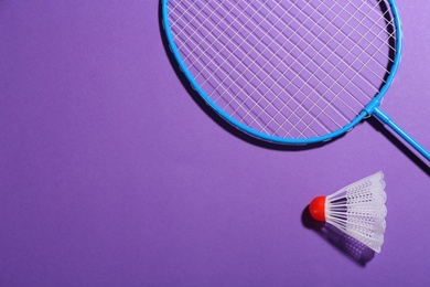 Photo of Badminton racket and shuttlecock on purple background, flat lay. Space for text