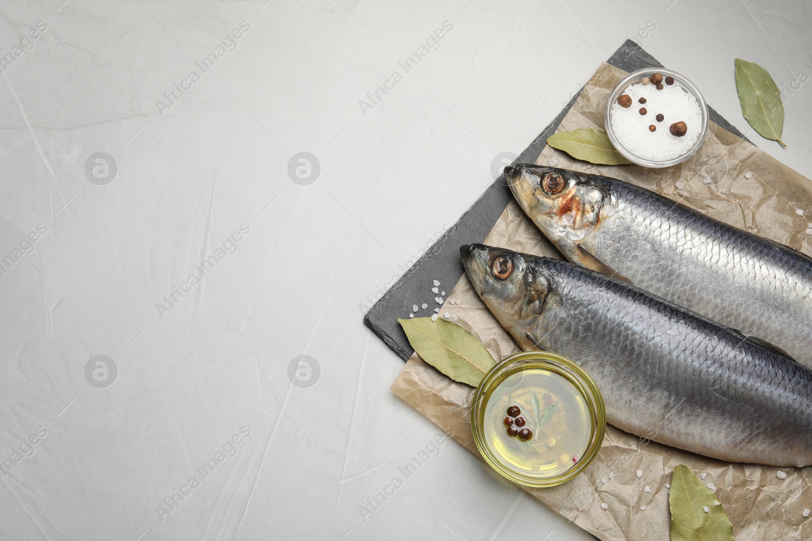 Photo of Slate plate with salted herrings, oil and spices on grey table, top view. Space for text