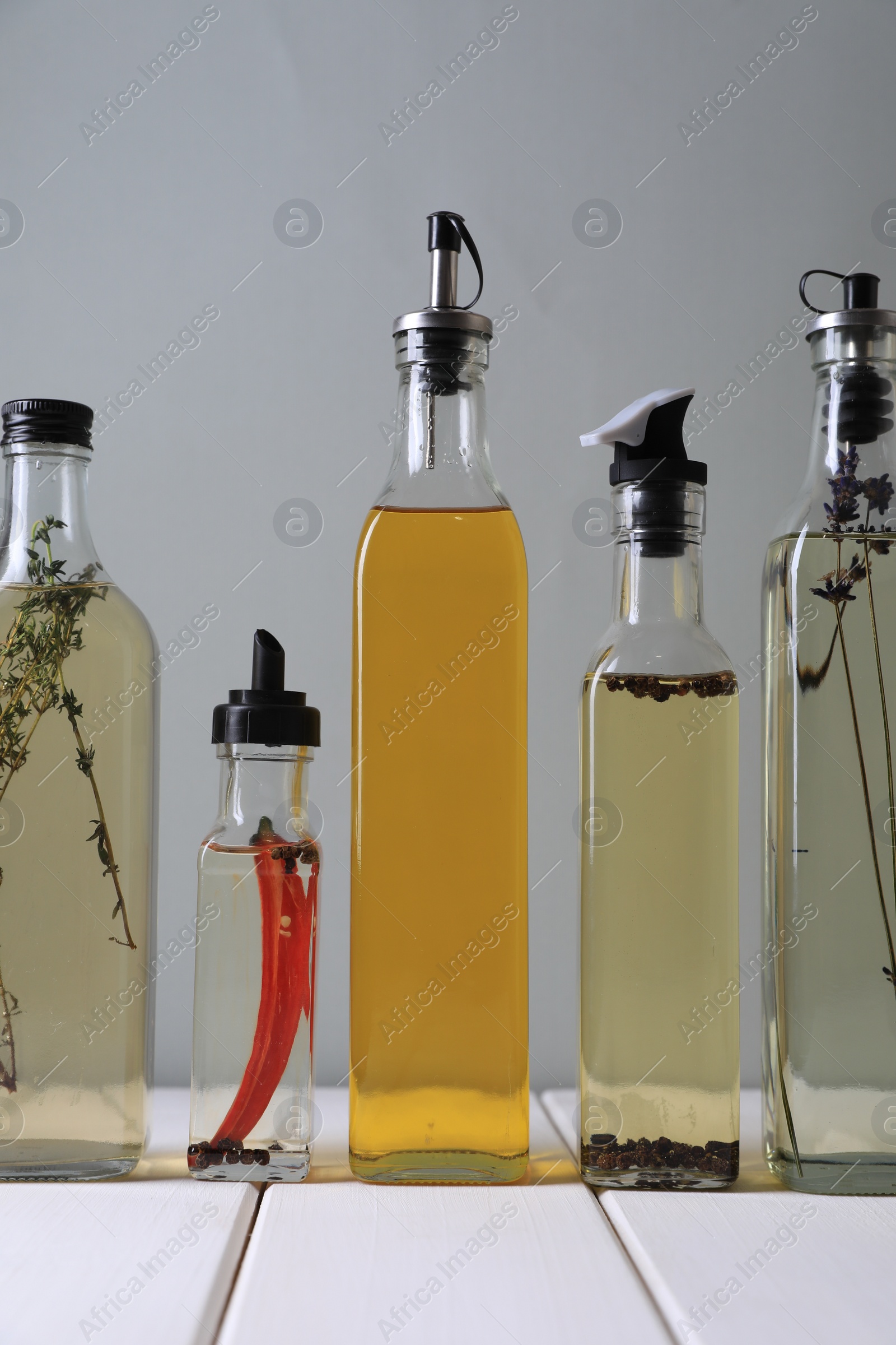 Photo of Bottles of different cooking oils on white wooden table against grey background