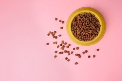Photo of Dry pet food in feeding bowl on pink background, top view. Space for text