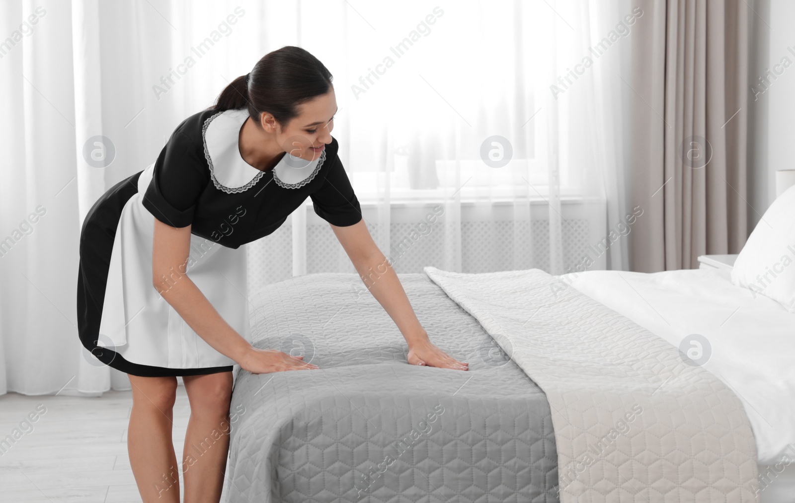 Photo of Young maid making bed in hotel room