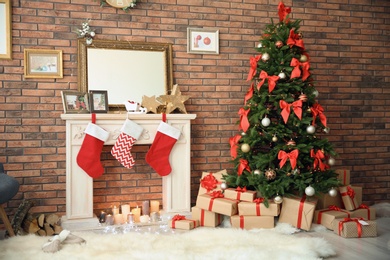 Photo of Beautiful Christmas tree and gifts near decorative fireplace with stockings indoors