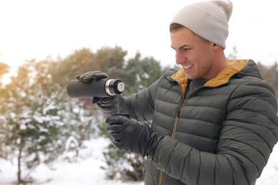 Photo of Man pouring hot drink from thermos into cap outdoors on snow day