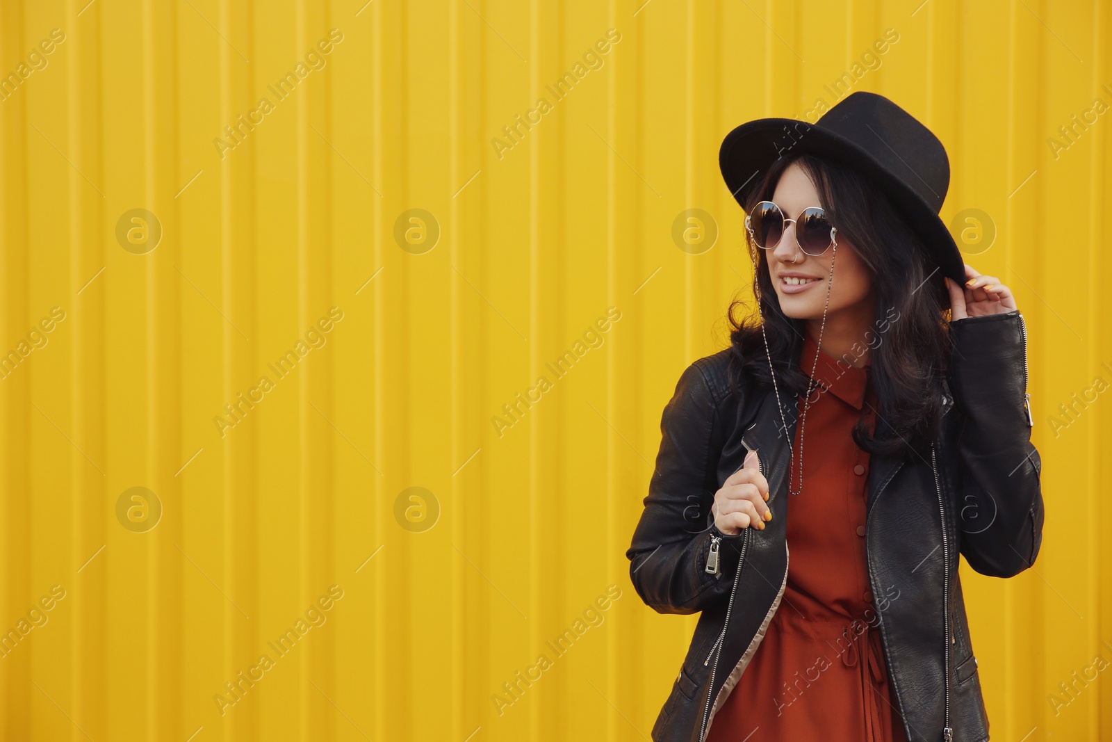 Photo of Beautiful young woman in stylish autumn clothes near yellow fence. Space for text