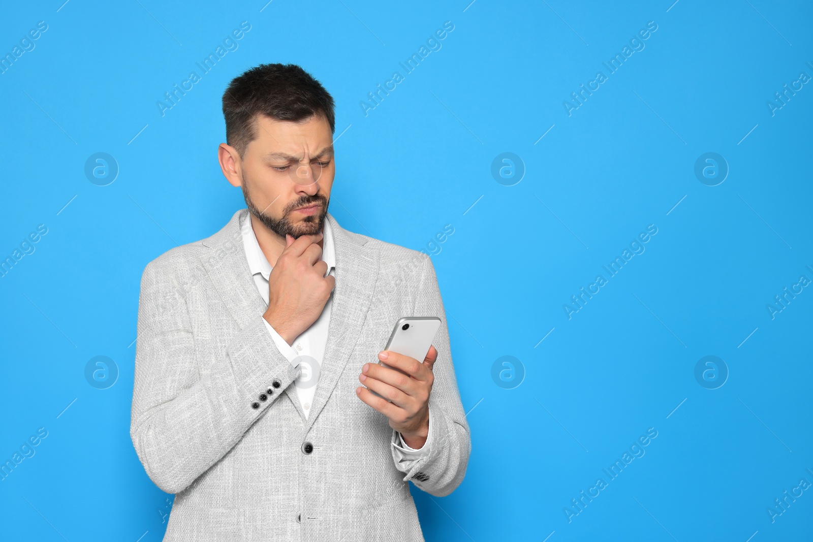 Photo of Pensive man looking at smartphone on light blue background. Space for text